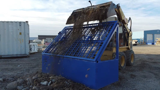 Skid steer dumping rocky soil onto a blue Bear Iron Works Growler grizzly rock screen.