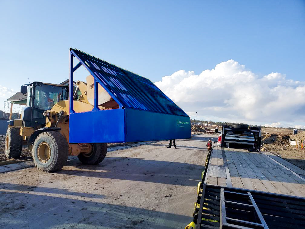 A loader lifting a large grizzly rock screen on a construction site.